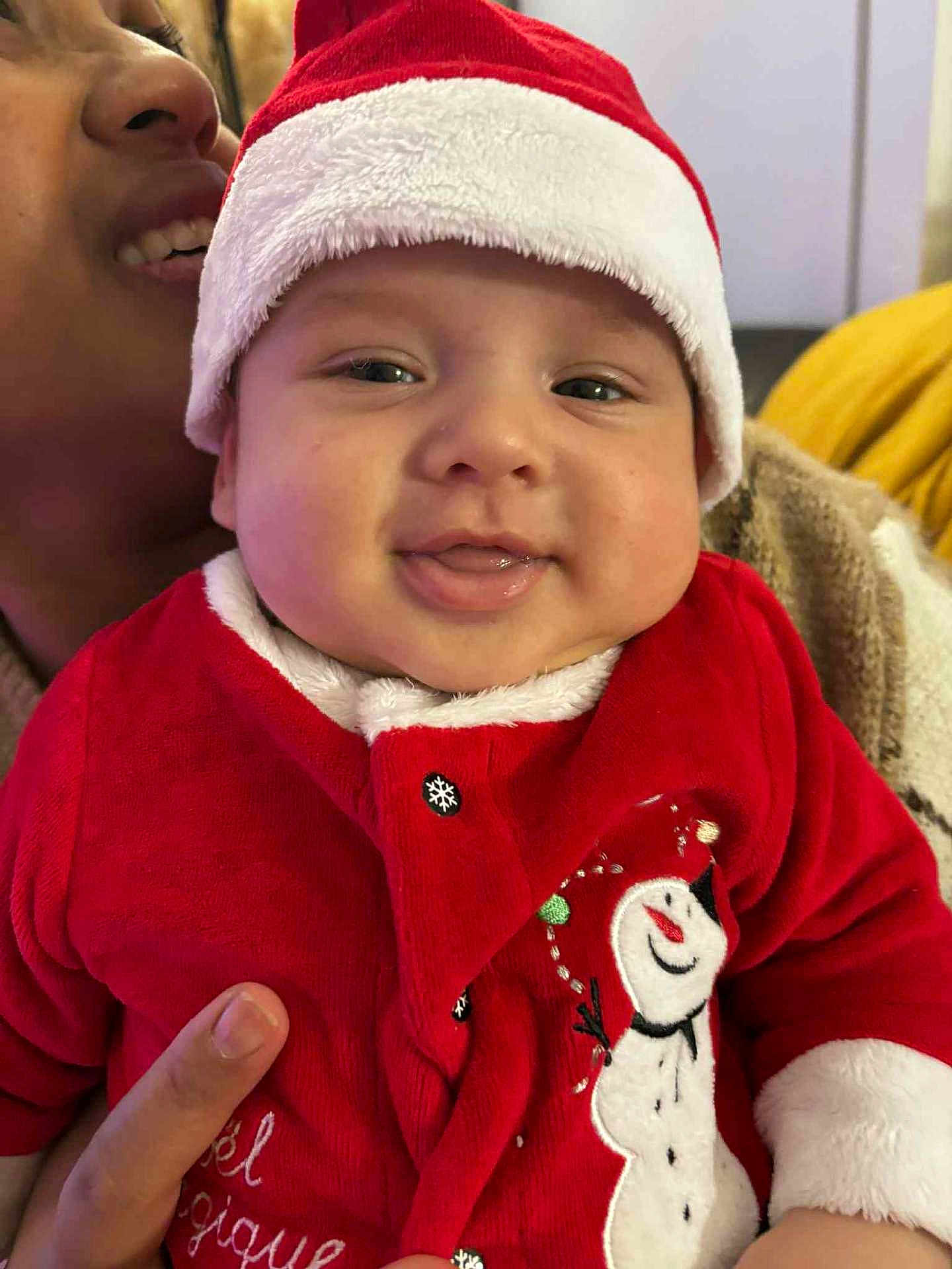 Aroon a rejoint le concours — aidez-le/la à gagner de superbes lots ! baby, child, smiling, face, red_clothing, santa_hat, holiday, festive, snowman, winter_wear, person, indoor, portrait, cute, happy, adult, hand, cozy, warm_clothing, closeup