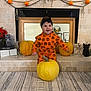 baby, child, pumpkin, halloween, orange_clothing, smile, headband, fireplace, decorations, skeleton, mirror, flowers, black_cat_figurine, floor, carpet, home_interior, festive, holiday, cute, person