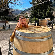 Lisandro a rejoint le concours — aidez-le/la à gagner de superbes lots ! child, smiling, barrel, outdoor, daylight, tree, blue_sky, stool, wood, seat, fence, mountain, glass_jar, playful, happy, casual_clothing, nature, sunlight, person, portrait