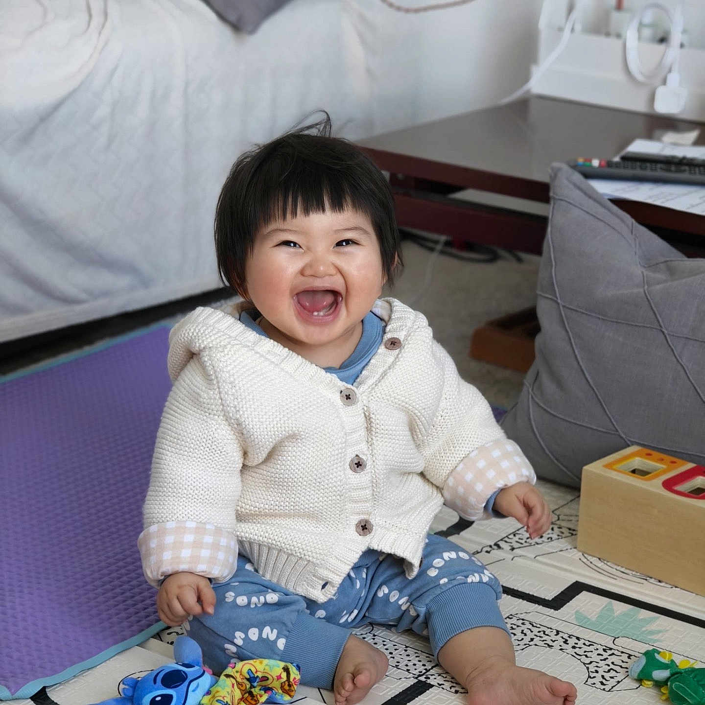 Isabella a rejoint le concours — aidez-le/la à gagner de superbes lots ! toddler, child, smiling, happy, indoor, toy, playmat, sweater, pants, barefoot, cushion, table, remote_control, plush_toy, colorful, floor, baby, cute, joy, home