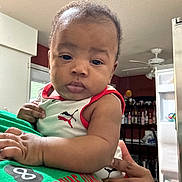 Zaylen is registered to the contest to win money with this photo: baby, bottle, casual, ceiling_fan, child, clothing, curious, expression, face, hand, holding, home, indoor, kitchen, person, person_holding, portrait, refrigerator, sleeveless_shirt, text_on_clothing
