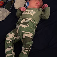 Atlas is registered to the contest to win money with this photo: baby, bed, camo_clothing, clothing, cute, dark_bedspread, diaper, footed_pajamas, indoors, infant, levis, lying_down, newborn, pacifier, phone, pouch, red_pouch, sleep, sleeping, yellow_spots