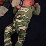 baby, bed, camo_clothing, clothing, cute, dark_bedspread, diaper, footed_pajamas, indoors, infant, levis, lying_down, newborn, pacifier, phone, pouch, red_pouch, sleep, sleeping, yellow_spots
