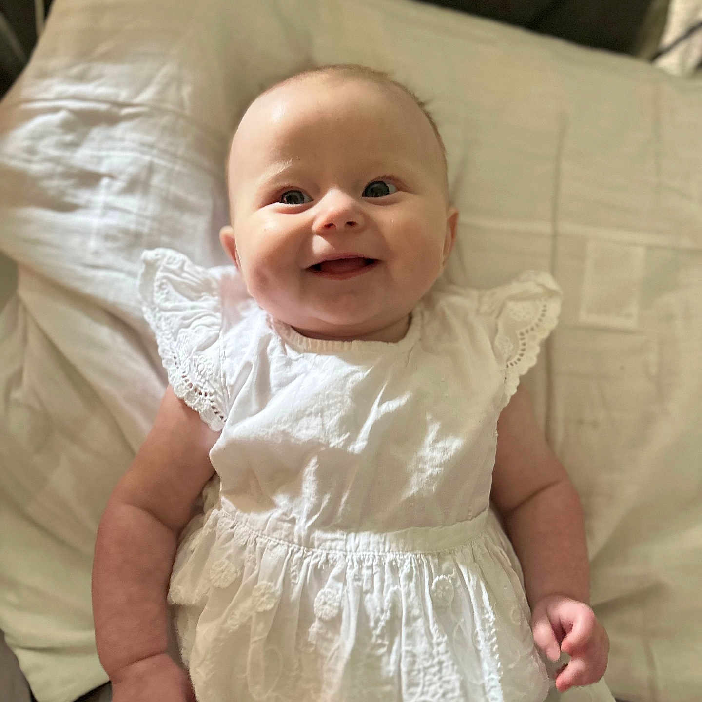 Ariana is registered to the contest to win money with this photo: adorable, baby, baby_girl, bed, child, cute, face, happy, indoor, infant, lying_down, person, pillow, portrait, skin, small_hands, smiling, soft_light, white_dress, young