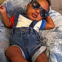Karter is registered to the contest to win money with this photo: baby, child, sunglasses, denim_overalls, blue_shirt, red_sleeve, blanket, soft_fabric, couch, tufted_headboard, footwear, sneakers, relaxed, indoor, portrait, cute, infant, fashion, casual, smiling