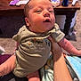 Adrastos is registered to the contest to win money with this photo: arm, baby, blanket, carpet, child, clothing, face, furniture, hand, holding, indoor, infant, living_room, onesie, person, skin, soda_can, table, toy, wooden_table