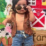 Ian is registered to the contest to win money with this photo: child, boy, sunglasses, vest, denim_shorts, cowboy_boots, cowboy, farm_backdrop, barn, cow, greenery, chain_necklace, posing, indoor, cute, serious_expression, short_hair, toy_theme, playful, colorful