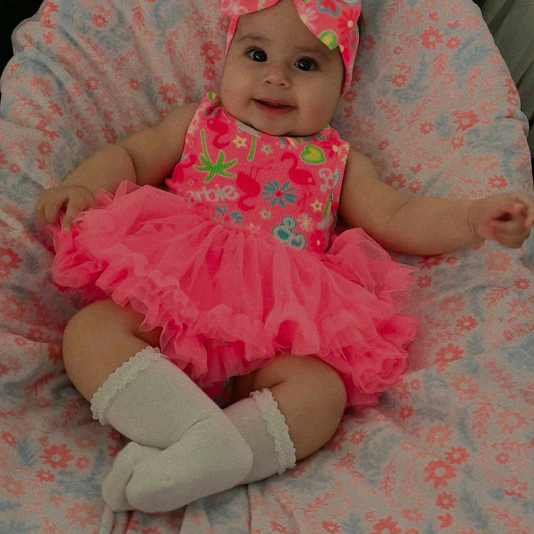 Nicolette joined the competition — help win amazing prizes! adorable, baby, blanket, child, clothing, comfortable, cute, floral_pattern, happy, headband, indoors, infant, person, pink_dress, portrait, sitting, smile, socks, soft_fabric, tutu