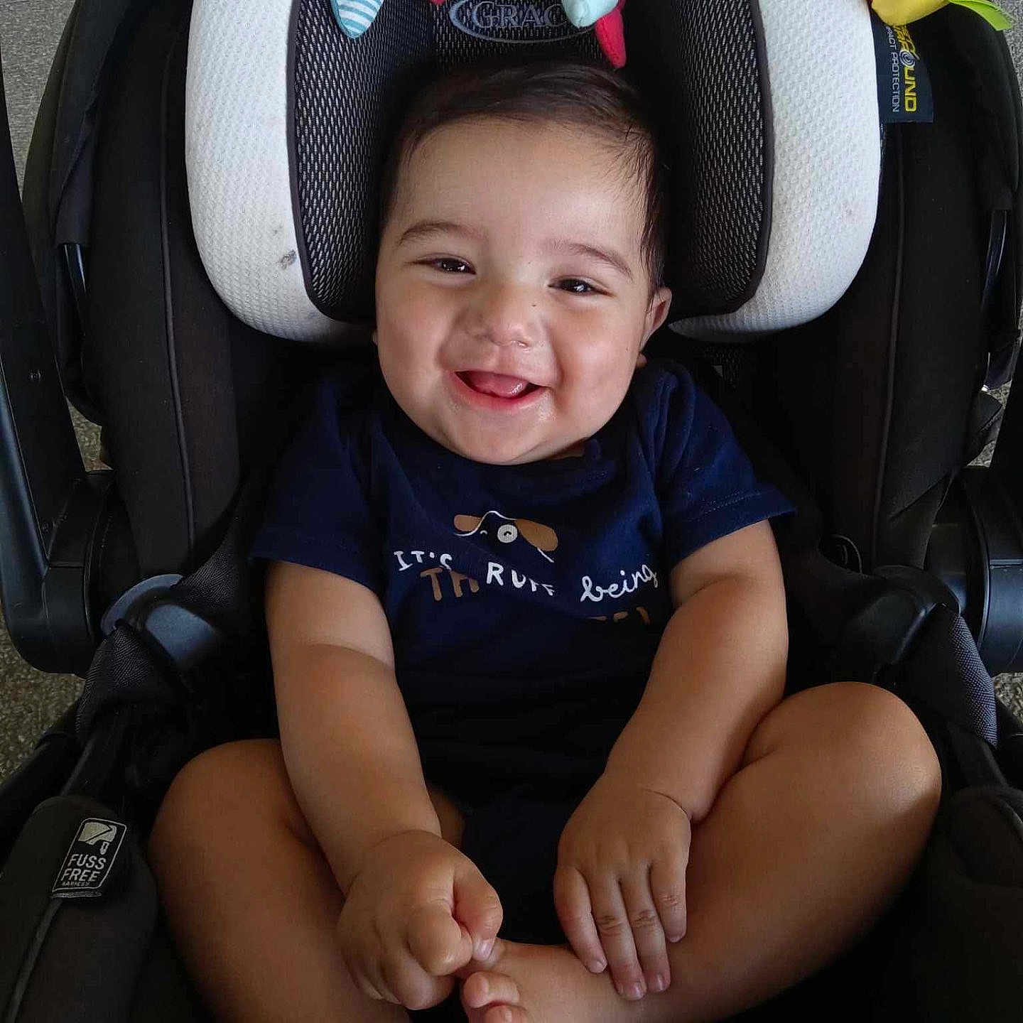 Marcus is registered to the contest to win money with this photo: baby, baby_toys, car_seat, child, clothing, comfort, cute, foot, grinning, hand, happy, head_support, indoor, infant, infant_clothing, person, safety, seat, smile, toy