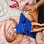 baby, blue_dress, pink_blanket, infant, child, person, hand, nail_polish, adult, soft_texture, bed, relaxing, cute, lying_down, tender_moment, skin, blanket, comfort, family, indoor