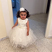 Jannah participe au concours pour gagner de l'argent avec cette photo : child, girl, dress, white_dress, flower_headband, curly_hair, indoor, hallway, tile_floor, doorway, smiling, person, cute, fashion, portrait, young_child, floor, wall, headwear, celebration
