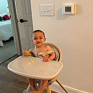 Derian joined the competition — help win amazing prizes! baby, high_chair, food, smiling, indoor, wooden_floor, door, bedroom, baby_food, child, person, modern_furniture, wall, thermostat, light_switch, happy, cute, infant, home, casual
