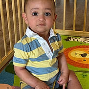 Derian is registered to the contest to win money with this photo: toddler, child, striped_shirt, play_mat, lion_image, wooden_bars, playpen, floor, indoor, curious_expression, sitting, cross_legged, short_hair, big_eyes, casual_clothing, colorful, young_child, baby, person, portrait