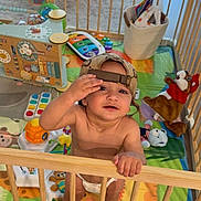 Derian is registered to the contest to win money with this photo: baby, child, playpen, toys, diaper, cap, indoor, colorful, basket, stuffed_animal, floor_mat, wooden_bars, smiling, cute, play, infant, happy, person, home, baby_toys