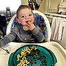 toddler, high_chair, macaroni, peas, food, kitchen, stove, towel, smiling, child, plate, utensil, meal, indoor, person, happy, eating, clothing, face, table