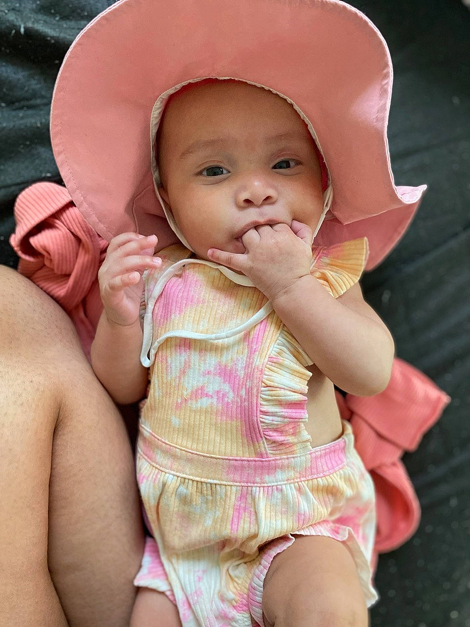 Esme is registered to the contest to win money with this photo: baby, baby_toddler_clothing, cheek, chin, comfort, eye, face, finger, happy, hat, head, human_body, iris, lip, mouth, nose, person, pink, skin, smile