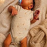 baby, infant, pacifier, blanket, knitted_hat, onesie, socks, lying_down, cozy, soft_texture, warm_lighting, cute, sleepy, child, indoors, relaxing, small_person, fuzzy_blanket, comfortable, peaceful