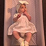baby, child, infant, white_dress, headband, socks, shoes, changing_pad, quilted, carpet, cute, lying_down, indoors, portrait, adorable, curious, hand, finger, soft_lighting, young_child