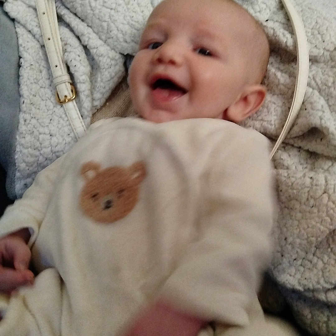Eliot a rejoint le concours — aidez-le/la à gagner de superbes lots ! baby, child, smiling, infant, clothing, teddy_bear_patch, blanket, bag, indoor, happy, face, person, cute, soft_texture, seated, portrait, cozy, warm, light_color, casual