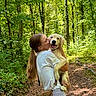 bag, casual_clothing, dog, forest, greenery, happy, holding, kiss, leash, long_hair, nature, outdoor, path, pet, puppy, smile, summer, sunlight, trees, woman