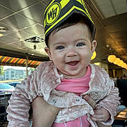 Audriana is registered to the contest to win money with this photo: baby, cheerful, child, cute, daylight, diner, face, hand, happy, hat, indoor, jacket, joyful, person, pink_clothing, portrait, smiling, table, watch, window