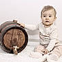 baby, child, infant, wooden_barrel, tap, white_blanket, sitting, curious, blue_eyes, long_sleeve_shirt, pants, sock, indoor, soft_light, portrait, cute, hand, face, expression, background