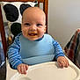 Koby joined the competition — help win amazing prizes! baby, high_chair, bib, food, messy_face, blue_shirt, smiling, happy, infant, child, indoor, wooden_chair, feeding, cute, portrait, face, hands, table, home, person