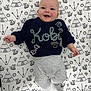 Koby joined the competition — help win amazing prizes! baby, smiling, sweater, knitted, name, lying_down, blanket, patterned, teepee, fox, arrow, sun, gray_pants, white_socks, happy, infant, cute, child, indoors, portrait
