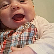 Cristian is registered to the contest to win money with this photo: baby, smiling, close_up, plaid_clothing, hand, infant, joyful, face, cheerful, cute, child, young, portrait, happy, skin, button, clothing, indoor, head, person