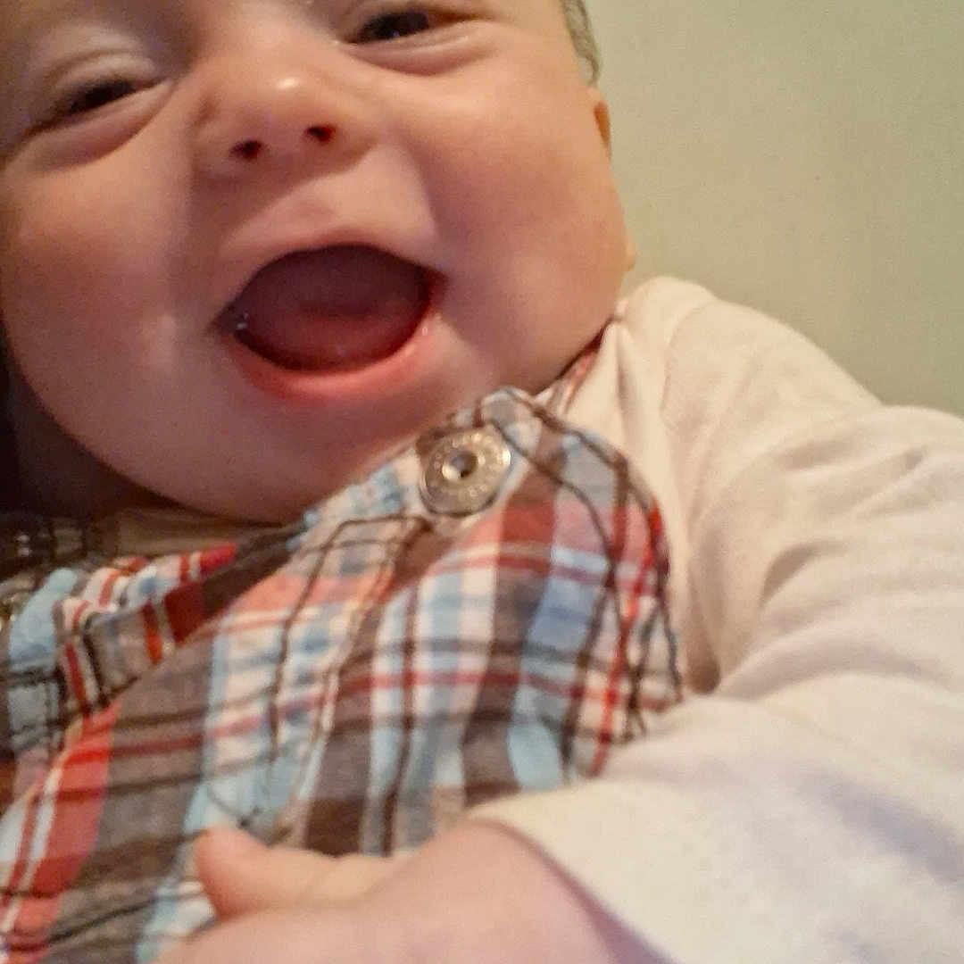 Cristian is registered to the contest to win money with this photo: baby, button, cheerful, child, close_up, clothing, cute, face, hand, happy, head, indoor, infant, joyful, person, plaid_clothing, portrait, skin, smiling, young