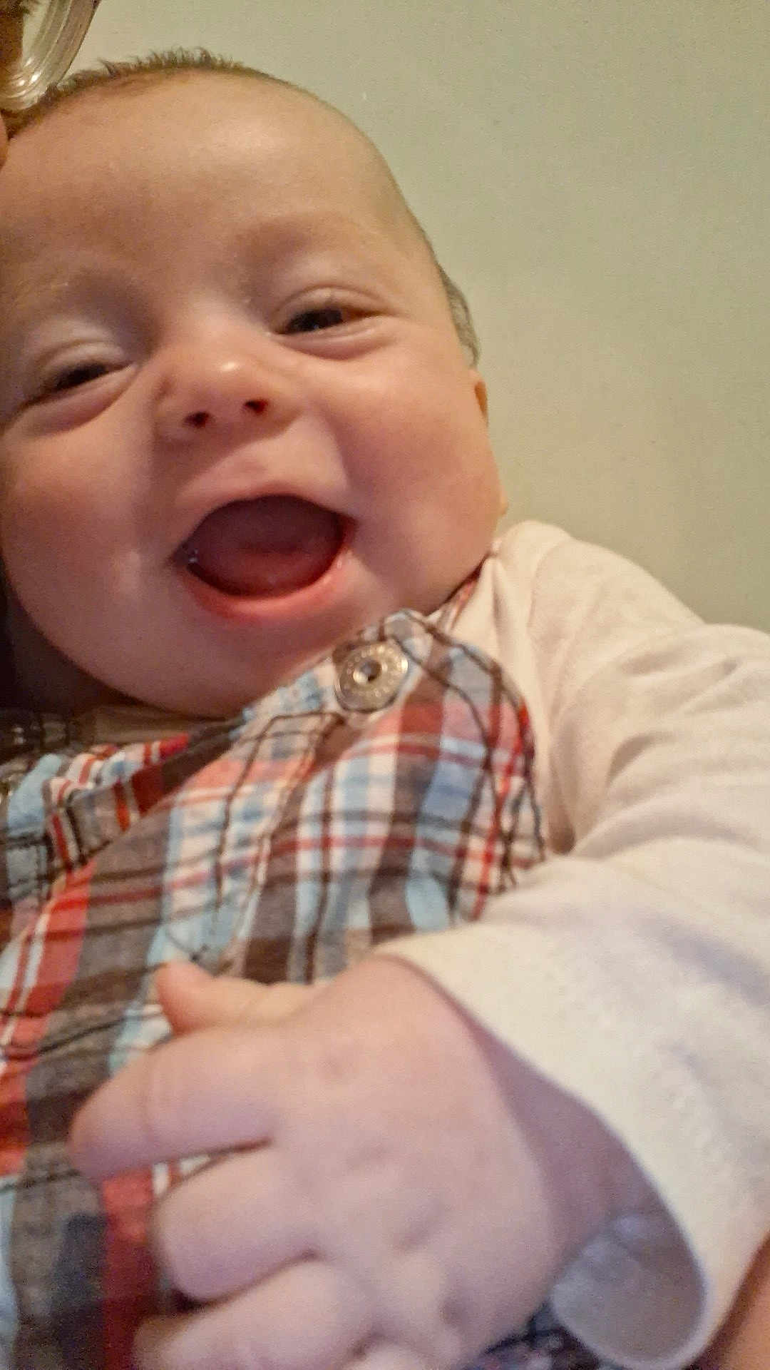 Cristian is registered to the contest to win money with this photo: baby, smiling, close_up, plaid_clothing, hand, infant, joyful, face, cheerful, cute, child, young, portrait, happy, skin, button, clothing, indoor, head, person