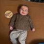 baby, infant, smiling, sweater, pants, socks, blanket, wooden_sign, three_months, lying_down, indoors, cute, child, portrait, cozy, happy, face, person, young_child, clothing