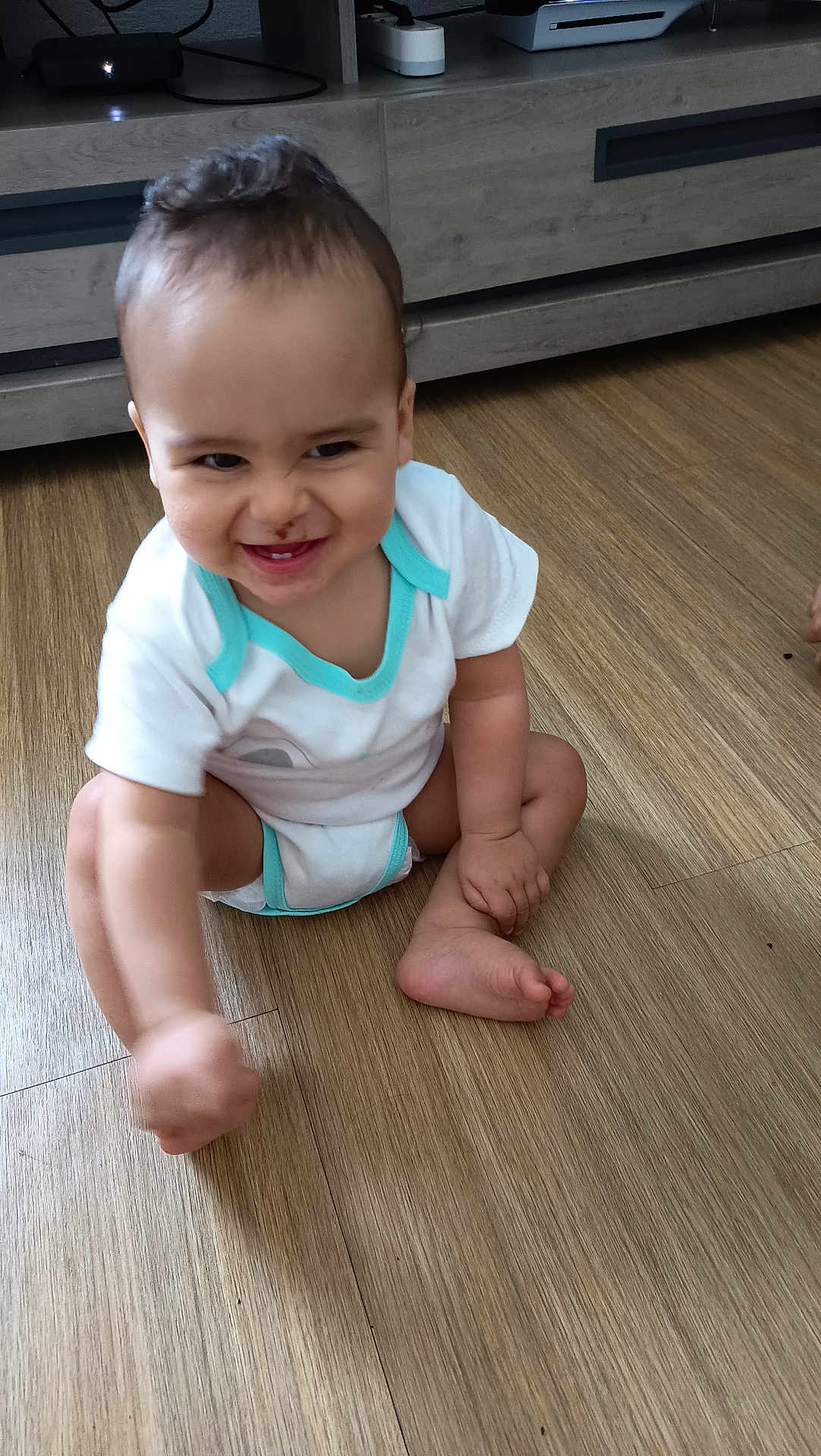 Aaron participe au concours pour gagner de l'argent avec cette photo : toddler, child, baby, onesie, floor, wooden_floor, smile, grin, indoor, furniture, cabinet, playful, crawling, happy, cute, person, infant, skin, head, hand