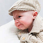 Davey is registered to the contest to win money with this photo: baby, infant, child, face, headwear, cap, shirt, clothing, pattern, houndstooth, cute, portrait, closeup, skin, ear, button, lying_down, soft_surface, expression, curious