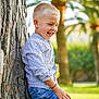 child, boy, smiling, outdoor, tree, nature, grass, casual_clothing, denim_shorts, striped_shirt, happy, blond_hair, sunlight, park, palm_trees, portrait, young, cute, joyful, leisure
