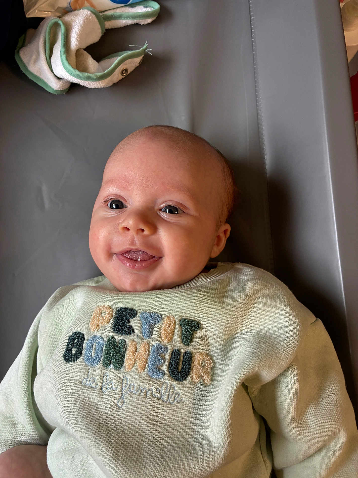 Théo a rejoint le concours — aidez-le/la à gagner de superbes lots ! baby, infant, smiling, face, eyes, tongue, sweater, clothing, embroidery, text, fabric, soft, lying, indoor, cute, child, person, portrait, head, happy