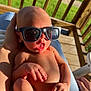 baby, sunglasses, infant, hand, foot, skin, outdoor, sunlight, wooden_deck, diaper, person, human, relaxing, cute, expression, summer, shadows, closeup, casual, holding