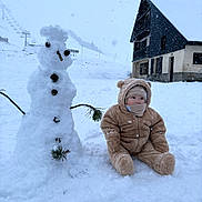 Teo participe au concours pour gagner de l'argent avec cette photo : child, toddler, snow, snowman, winter, snowy, mountain, ski_lift, house, building, pine_branch, pinecone, snowsuit, outdoor, cold, cute, playful, winter_clothing, sitting, face