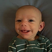 Jasper is registered to the contest to win money with this photo: baby, smiling, tongue_out, green_onesie, striped_clothing, infant, cute, portrait, face, happy, child, young, lying_down, head, skin, eyes, mouth, ear, indoor, soft_background