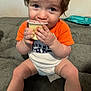 toddler, child, pudding, food, orange_shirt, white_onesie, couch, furniture, indoor, sitting, hands, face, legs, cute, snack, expression, eyes, hair, person, home