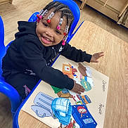 Tamia joined the competition — help win amazing prizes! child, smiling, beads, braids, blue_chair, table, educational_poster, donation, recycle, wooden_floor, indoor, happy, person, clothing, black_hoodie, small_table, learning, activity, colorful, cute