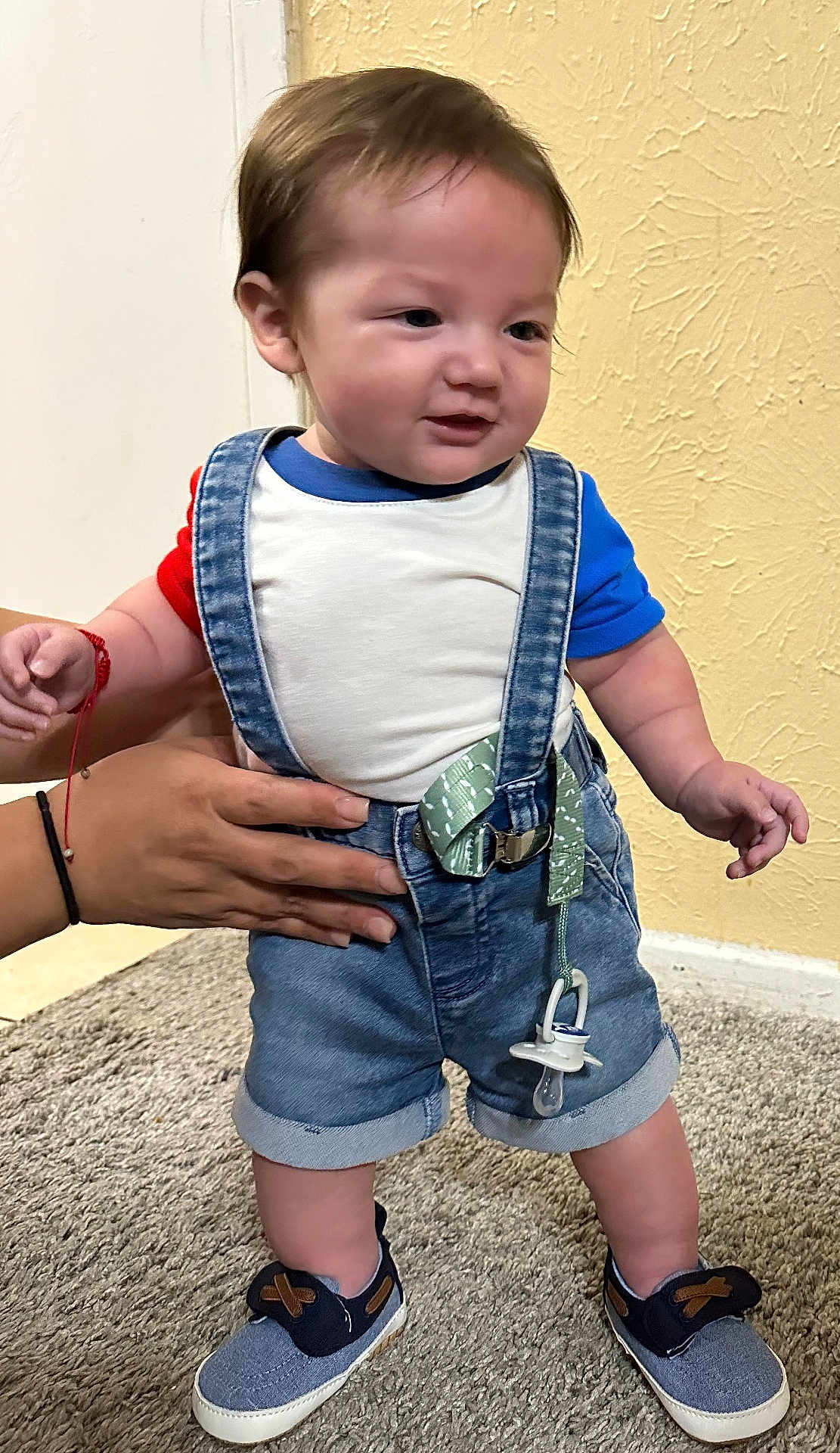 Manuel Maturino Jr is registered to the contest to win money with this photo: blue_shirt, carpet, child, clothing, cute, denim, footwear, hands, indoor, infant, pacifier, person, red_shirt, shoes, shorts, standing, suspenders, textured_wall, toddler, wall