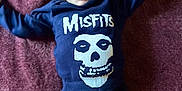 Lilith joined the competition — help win amazing prizes! baby, infant, blue_eyes, onesie, misfits, skull_logo, lying_down, purple_blanket, happy, smiling, raised_arms, clothing, small_person, cute, child, portrait, indoors, soft_texture, baby_garment, expressive_face