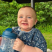 Wilder is registered to the contest to win money with this photo: baby, child, smiling, blue_eyes, sippy_cup, outdoor, greenery, umbrella, happy, tooth, clothing, short_sleeves, nature, table, person, infant, cute, face, hand, daylight