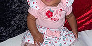 Unique is registered to the contest to win money with this photo: baby, child, infant, smiling, pink_clothing, dress, sitting, barefoot, curly_hair, face, portrait, cute, indoor, fabric, velvet, red_background, black_background, floral_pattern, ladybug, bow
