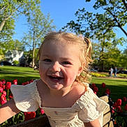 Averie is registered to the contest to win money with this photo: toddler, child, smiling, curly_hair, blonde_hair, outdoor, park, bench, flowers, tulips, spring, sunlight, greenery, happy, nature, daytime, grass, trees, dress, playful