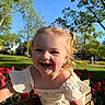 toddler, child, smiling, curly_hair, blonde_hair, outdoor, park, bench, flowers, tulips, spring, sunlight, greenery, happy, nature, daytime, grass, trees, dress, playful