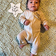 Milo is registered to the contest to win money with this photo: baby, infant, blanket, onesie, star_shaped_sign, milestone, lying_down, indoor, cute, portrait, face, hands, feet, text, milestone_marker, cozy, soft_texture, expression, young_child, newborn