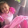 child, girl, smiling, portrait, car, seatbelt, vehicle, pink_dress, formalwear, ruffles, jewelry, headband, seated, indoors, automotive, sunlight, window, happy, fashion, toddler