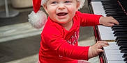 Graham joined the competition — help win amazing prizes! baby, child, piano, santa_hat, red_clothing, striped_pants, smiling, happy, indoors, music, musical_instrument, bench, holiday, christmas, cute, infant, playing, furniture, white_socks, floor